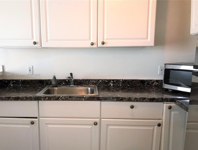 kitchen featuring a sink, stainless steel microwave, and white cabinetry