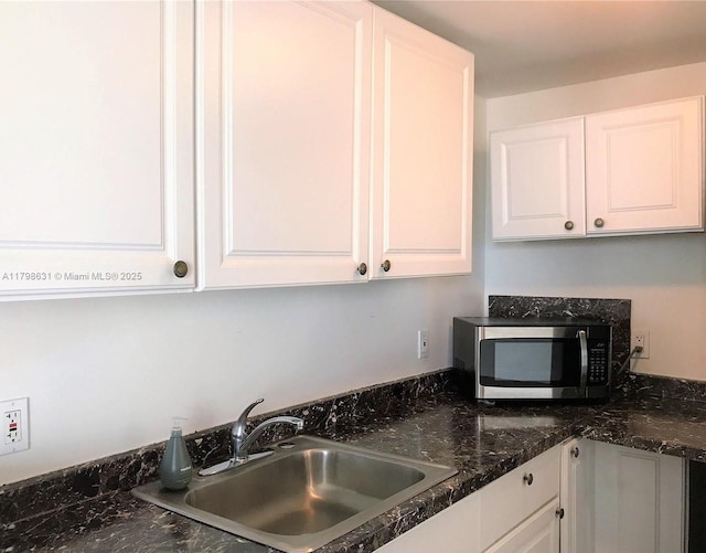 kitchen featuring stainless steel microwave, a sink, and white cabinetry