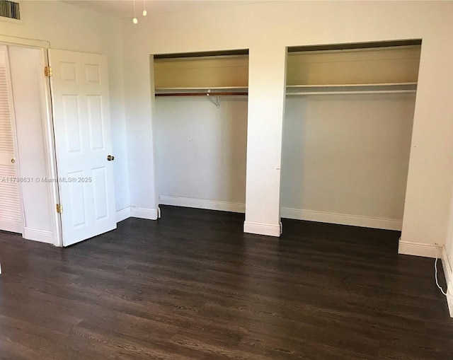 unfurnished bedroom with two closets, dark wood-type flooring, and baseboards