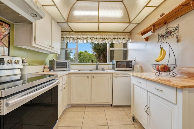 kitchen with appliances with stainless steel finishes, under cabinet range hood, a sink, light tile patterned floors, and butcher block countertops
