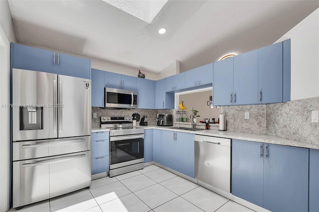 kitchen with appliances with stainless steel finishes, blue cabinetry, a sink, backsplash, and recessed lighting