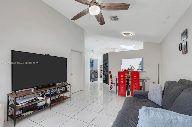 living area featuring vaulted ceiling, washing machine and dryer, a skylight, a ceiling fan, and light tile patterned flooring