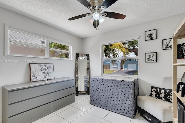 sitting room with healthy amount of natural light, a textured ceiling, ceiling fan, and light tile patterned floors
