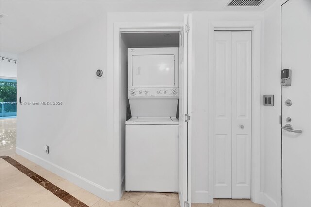 laundry area with stacked washer / dryer, baseboards, and light tile patterned floors
