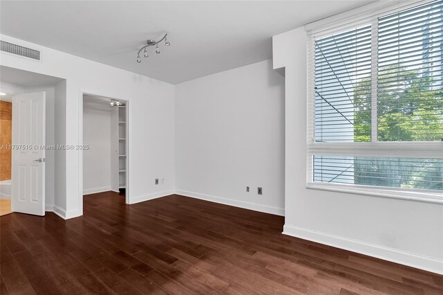 unfurnished bedroom with baseboards, wood finished floors, a spacious closet, a closet, and track lighting