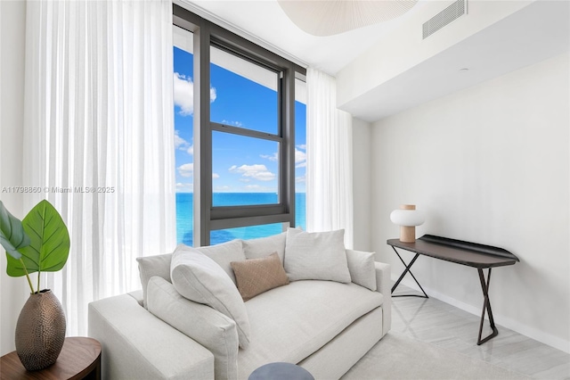 living area with baseboards, a water view, and expansive windows