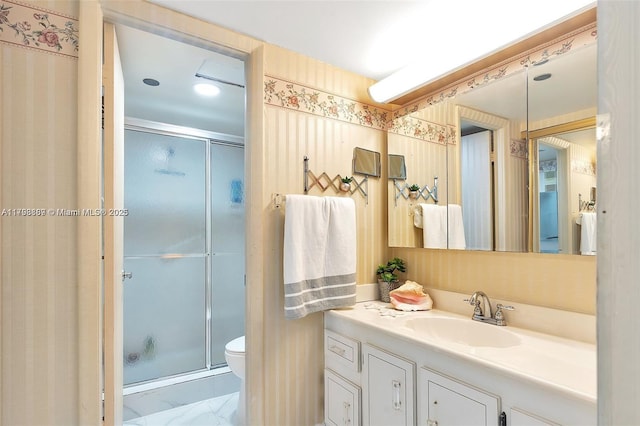 bathroom with a shower stall, marble finish flooring, vanity, toilet, and wallpapered walls