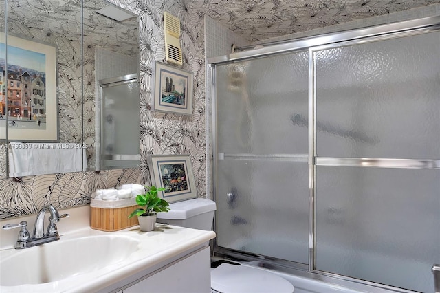 bathroom with wallpapered walls, toilet, vanity, and combined bath / shower with glass door