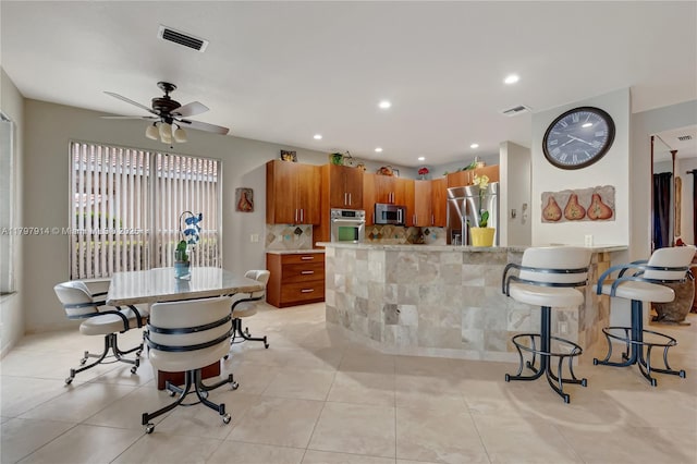 12672 Tucano Cir, Boca Raton, FL 33428 - kitchen featuring stainless steel appliances, brown cabinets, a ceiling fan, a kitchen bar, and light tile patterned floors