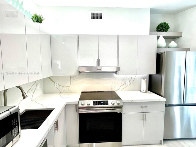 2406 Marathon Ln, Fort Lauderdale, FL 33312 - kitchen with stainless steel appliances, under cabinet range hood, decorative backsplash, open shelves, and light stone countertops