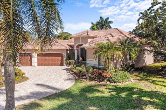 8100 Muirhead Cir, Boynton Beach, FL 33472 - mediterranean / spanish-style house featuring stucco siding, an attached garage, a tiled roof, decorative driveway, and a front lawn