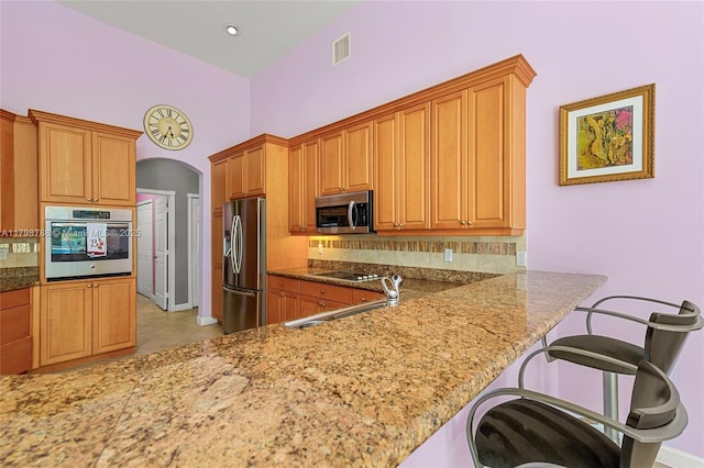 8100 Muirhead Cir, Boynton Beach, FL 33472 - kitchen with stainless steel appliances, light stone counters, arched walkways, light tile patterned flooring, and brown cabinets