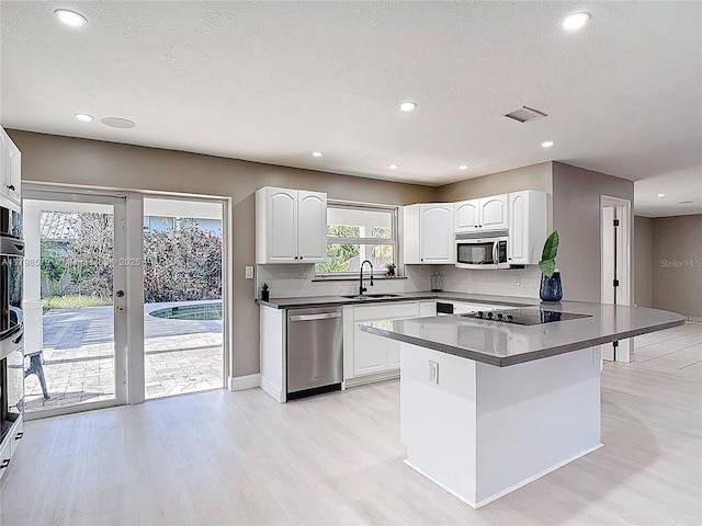 10227 SW 53rd Ct, Cooper City, FL 33328 - kitchen featuring stainless steel appliances, dark countertops, a sink, light wood finished floors, and white cabinets