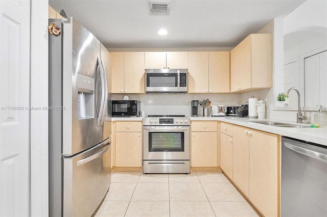 kitchen featuring appliances with stainless steel finishes, a sink, light brown cabinets, light tile patterned flooring, and recessed lighting