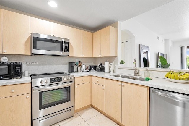 kitchen with appliances with stainless steel finishes, a sink, and light brown cabinetry