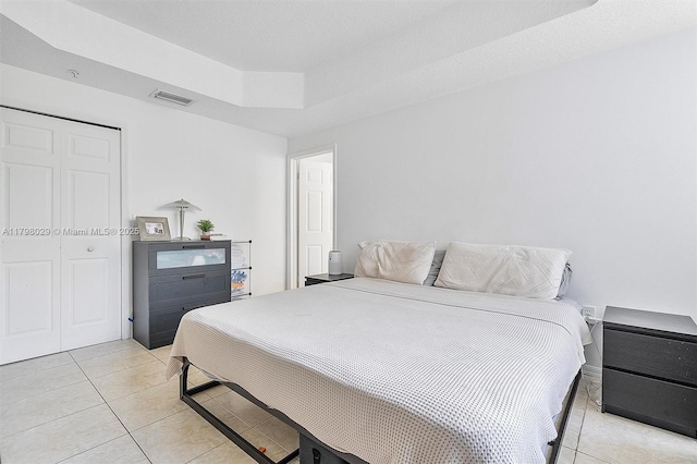 bedroom with light tile patterned flooring, a raised ceiling, and a closet