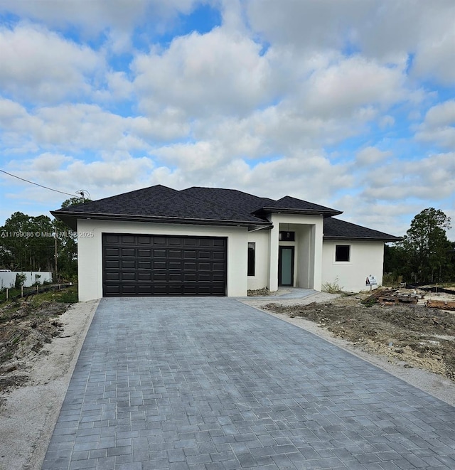 prairie-style home with stucco siding, an attached garage, and decorative driveway