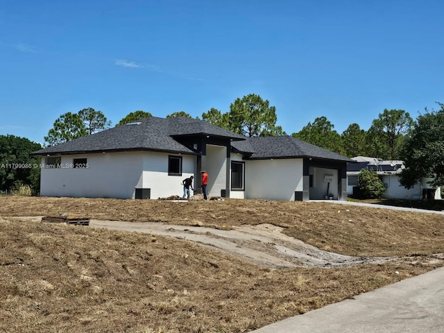 view of front facade with stucco siding, an attached garage, and roof with shingles
