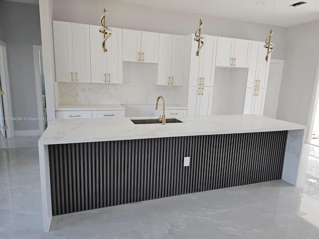 kitchen with a sink, tasteful backsplash, white cabinetry, a kitchen island with sink, and light stone countertops