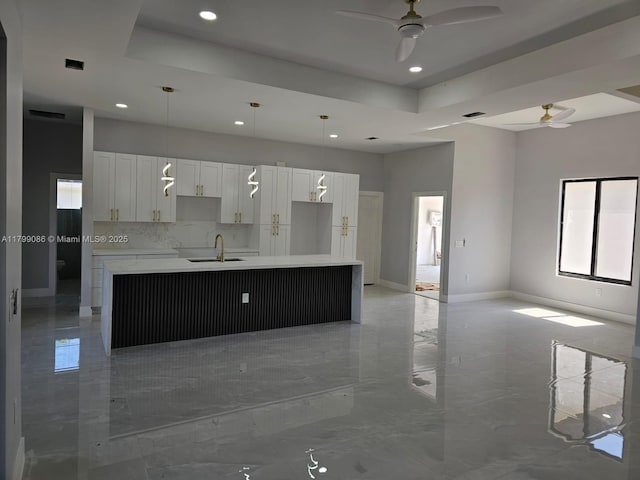 kitchen featuring ceiling fan, recessed lighting, a sink, an island with sink, and a raised ceiling