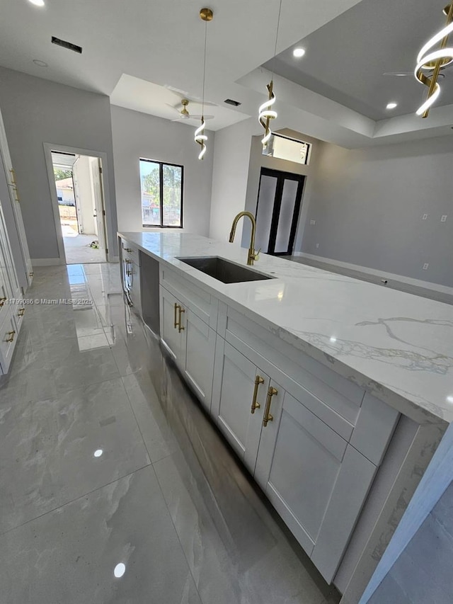 kitchen with a sink, white cabinetry, light stone countertops, pendant lighting, and recessed lighting