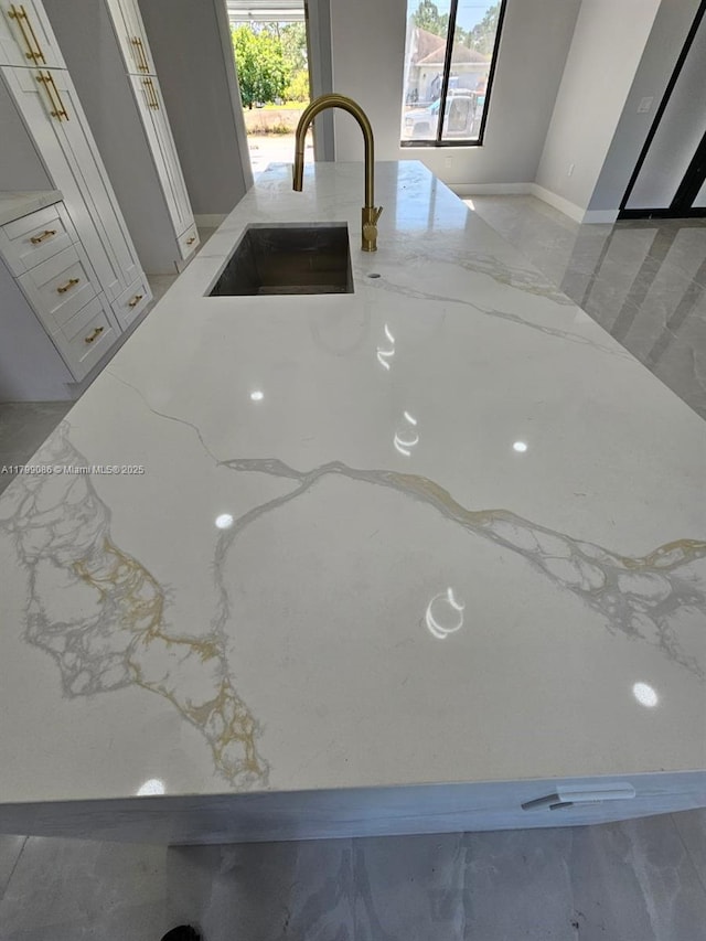 kitchen view of a sink, light stone countertops, and white cabinets