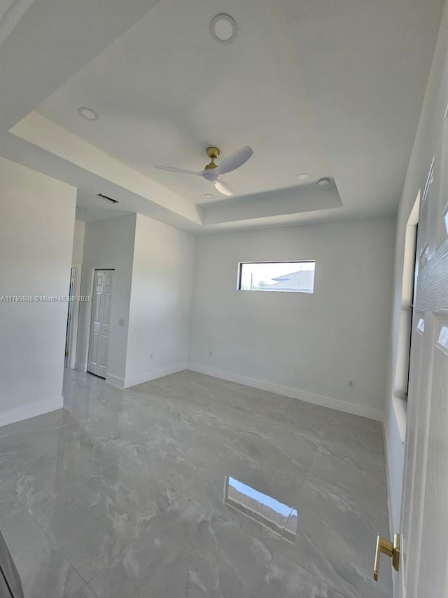 spare room with a tray ceiling, baseboards, a ceiling fan, and marble finish floors