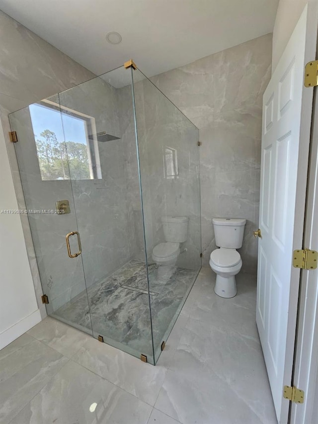 bathroom with marble tiled flooring, toilet, a stall shower, and tile walls