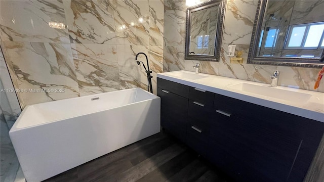 bathroom featuring tile walls, double vanity, wood finished floors, and a freestanding tub
