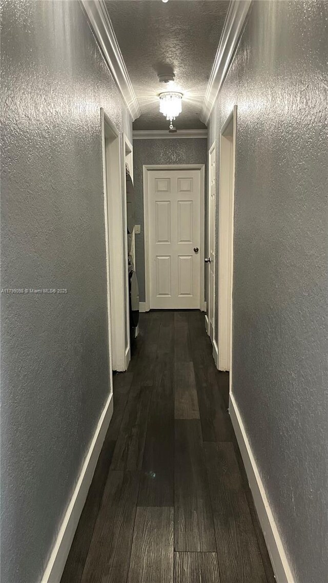 hall with ornamental molding, a textured wall, dark wood-type flooring, and baseboards