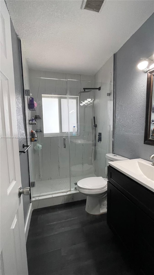 full bathroom featuring toilet, a textured ceiling, a marble finish shower, vanity, and wood finished floors