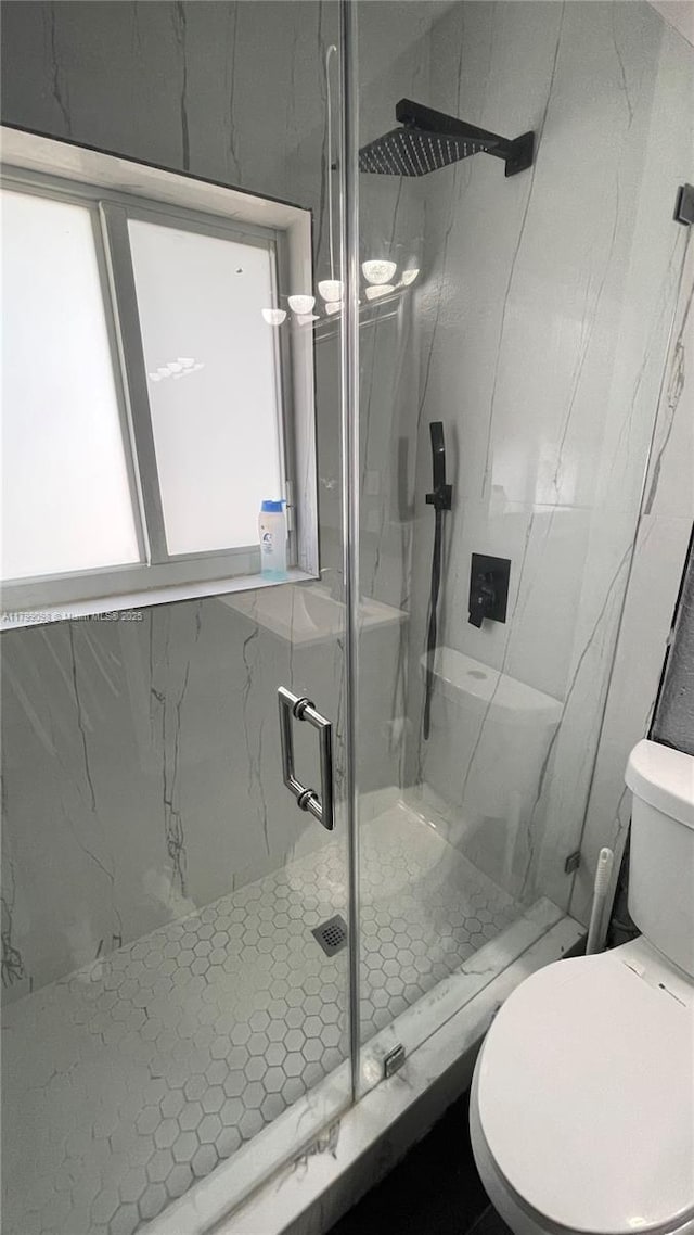 full bath featuring a marble finish shower, toilet, and healthy amount of natural light