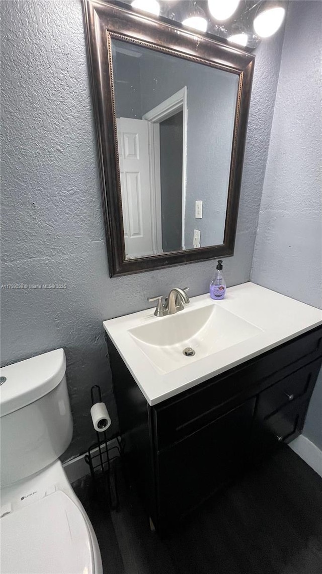 half bathroom featuring a textured wall, vanity, and toilet