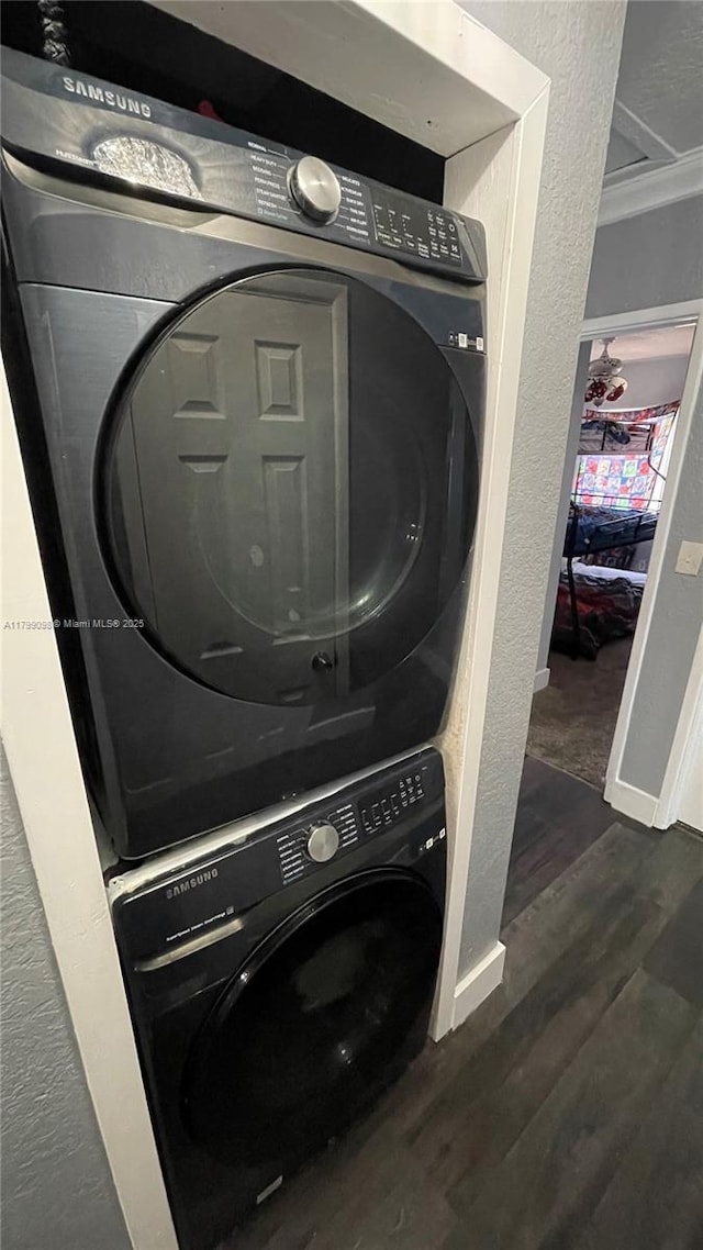 washroom with estacked washer and dryer, dark wood finished floors, a textured wall, ornamental molding, and baseboards