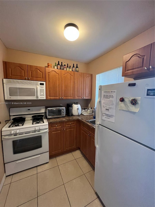 14500 SW 88th Ave Unit 245, Palmetto Bay, FL 33176 - kitchen featuring white appliances, light tile patterned floors, brown cabinetry, and dark countertops