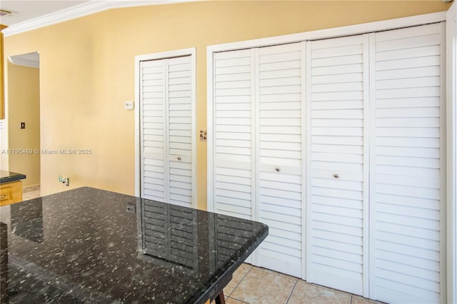 kitchen featuring crown molding, light tile patterned flooring, and dark stone counters