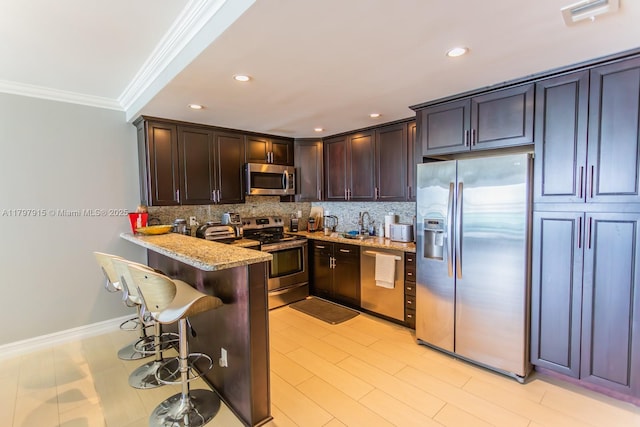 kitchen featuring appliances with stainless steel finishes, ornamental molding, tasteful backsplash, light stone countertops, and a kitchen bar
