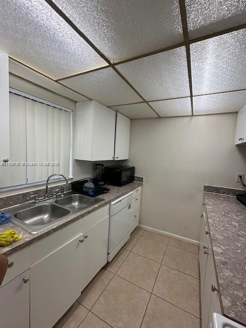2000 N Congress Ave Unit 411, West Palm Beach, FL 33401 - kitchen featuring a sink, black microwave, white cabinets, light tile patterned floors, and baseboards