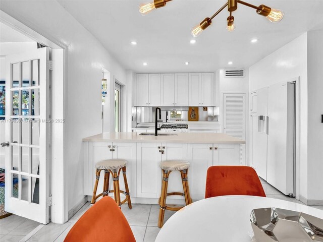 729 85th St, Miami Beach, FL 33141 - kitchen with a sink, white fridge, white cabinetry, light countertops, and a peninsula