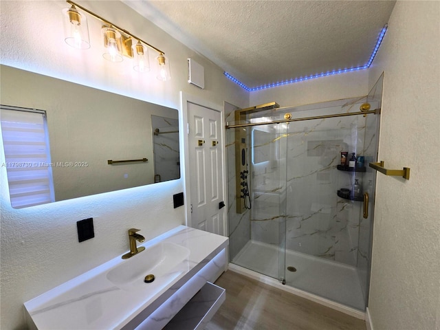 full bath with a textured ceiling, wood finished floors, a marble finish shower, vanity, and a textured wall