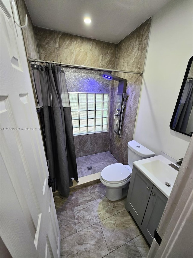 full bathroom featuring marble finish floors, a tile shower, toilet, and vanity