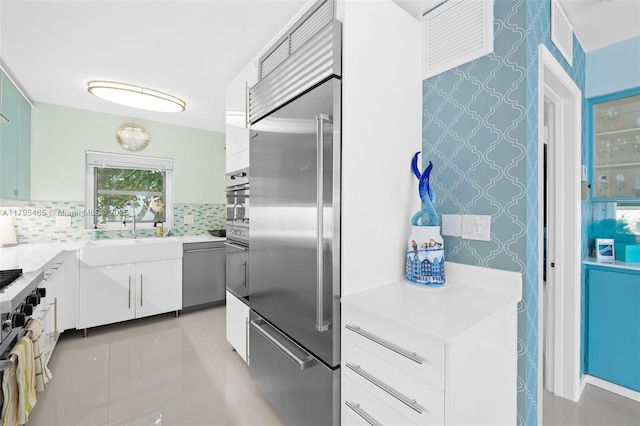kitchen featuring appliances with stainless steel finishes, decorative backsplash, light countertops, white cabinetry, and wallpapered walls