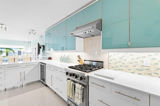 kitchen featuring stainless steel range, under cabinet range hood, beverage cooler, blue cabinets, and decorative backsplash