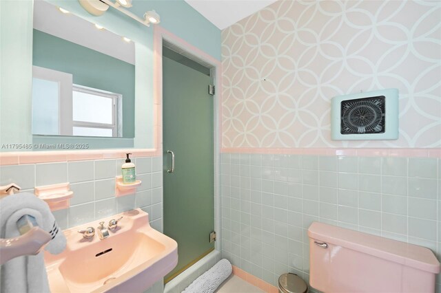 bathroom with tile walls, wallpapered walls, a shower stall, a sink, and a wainscoted wall