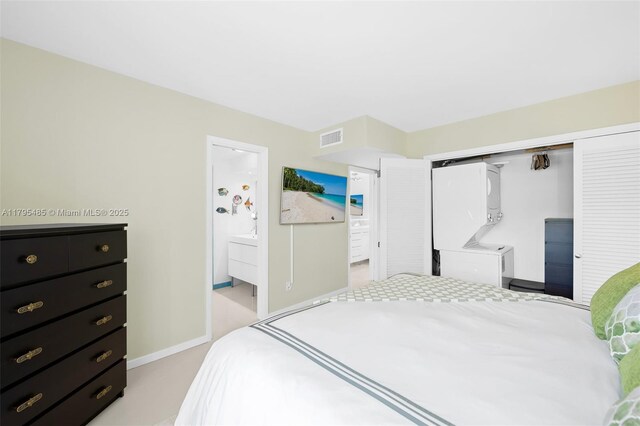bedroom featuring a closet, ensuite bath, light colored carpet, and baseboards