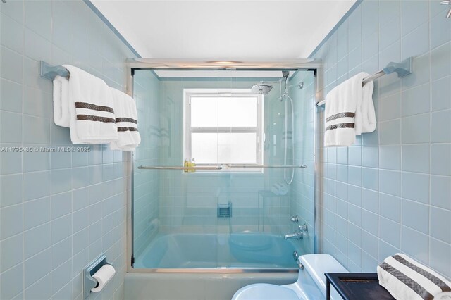 full bath with tile walls, toilet, and shower / bath combination with glass door