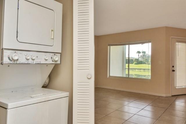 laundry room featuring stacked washer and clothes dryer, baseboards, and light tile patterned floors