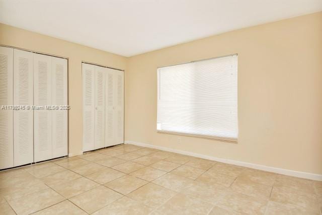 unfurnished bedroom with two closets, baseboards, and light tile patterned floors