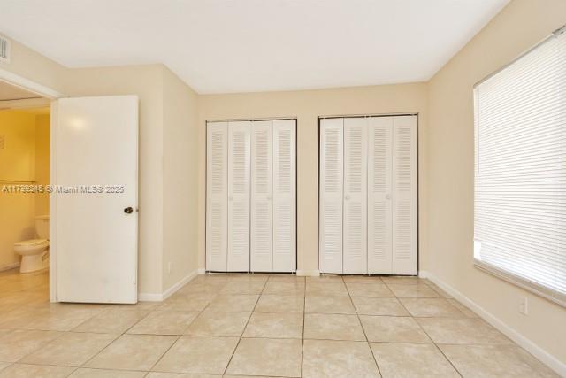 unfurnished bedroom featuring multiple closets, light tile patterned flooring, and baseboards