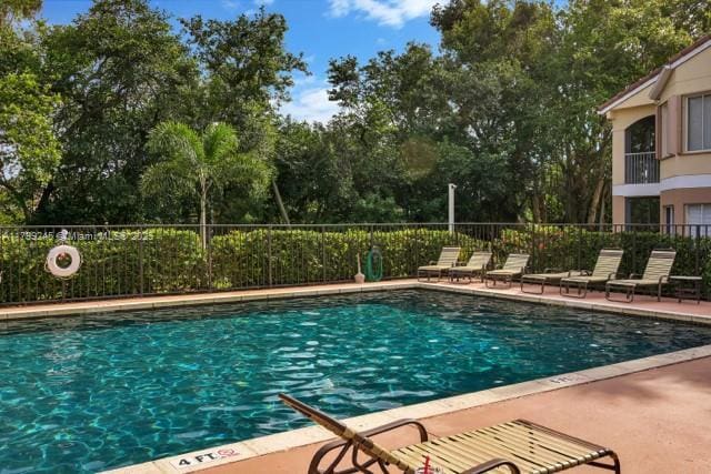 community pool with fence, a patio area, and view of scattered trees
